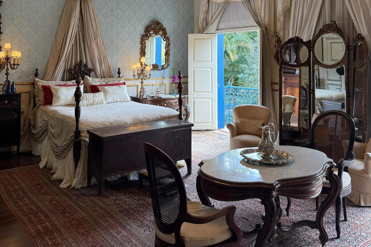 Une chambre à coucher luxueuse, dotée d’un lit à baldaquin, d’un lustre somptueux et d’un grand miroir.