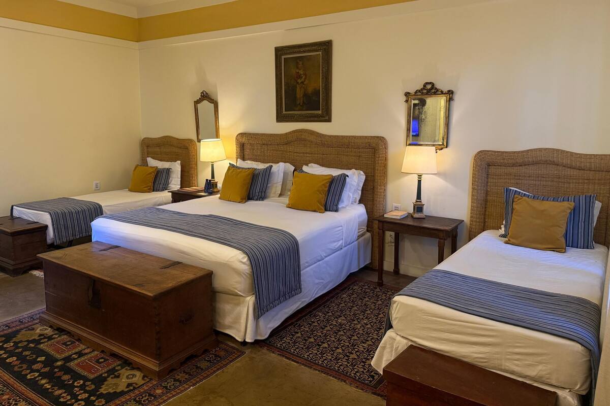 Une chambre d’hôtel avec deux lits simples, une commode en bois et un tapis à motifs.