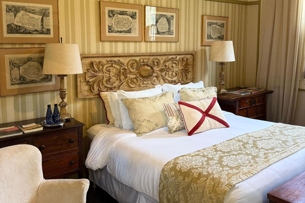 Une chambre d’hôtel avec un grand lit, deux tables de chevet, une petite table en bois, une chaise et un mur orné de tableaux.