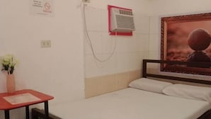 Hotelkamer met een bed, een kleine tafel met stoel, een wandairconditioner en een poster aan de muur.