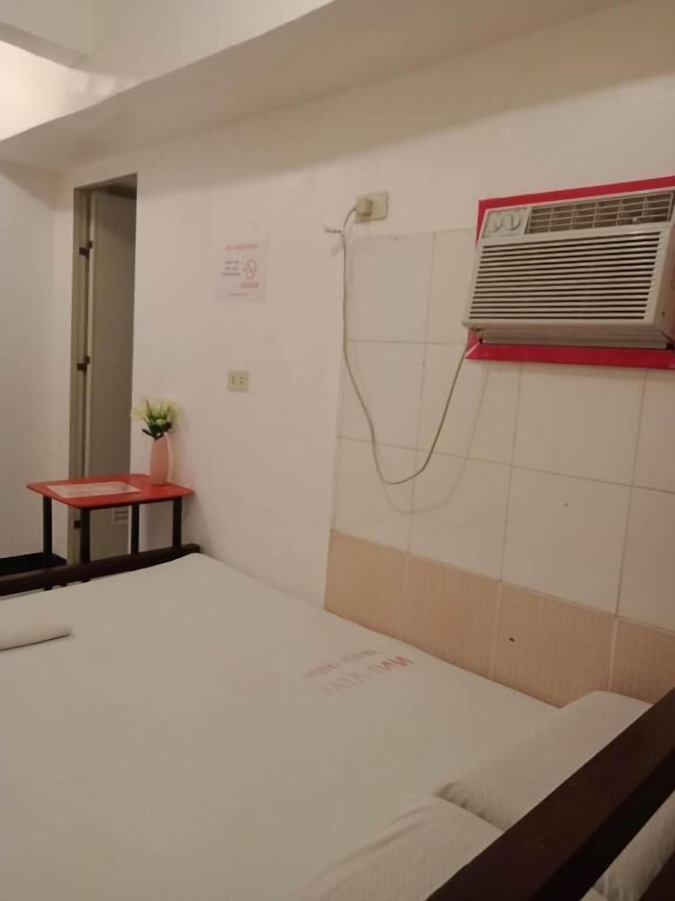 Una habitación con una cama, una mesita con una planta, un equipo de aire acondicionado y una ducha.
