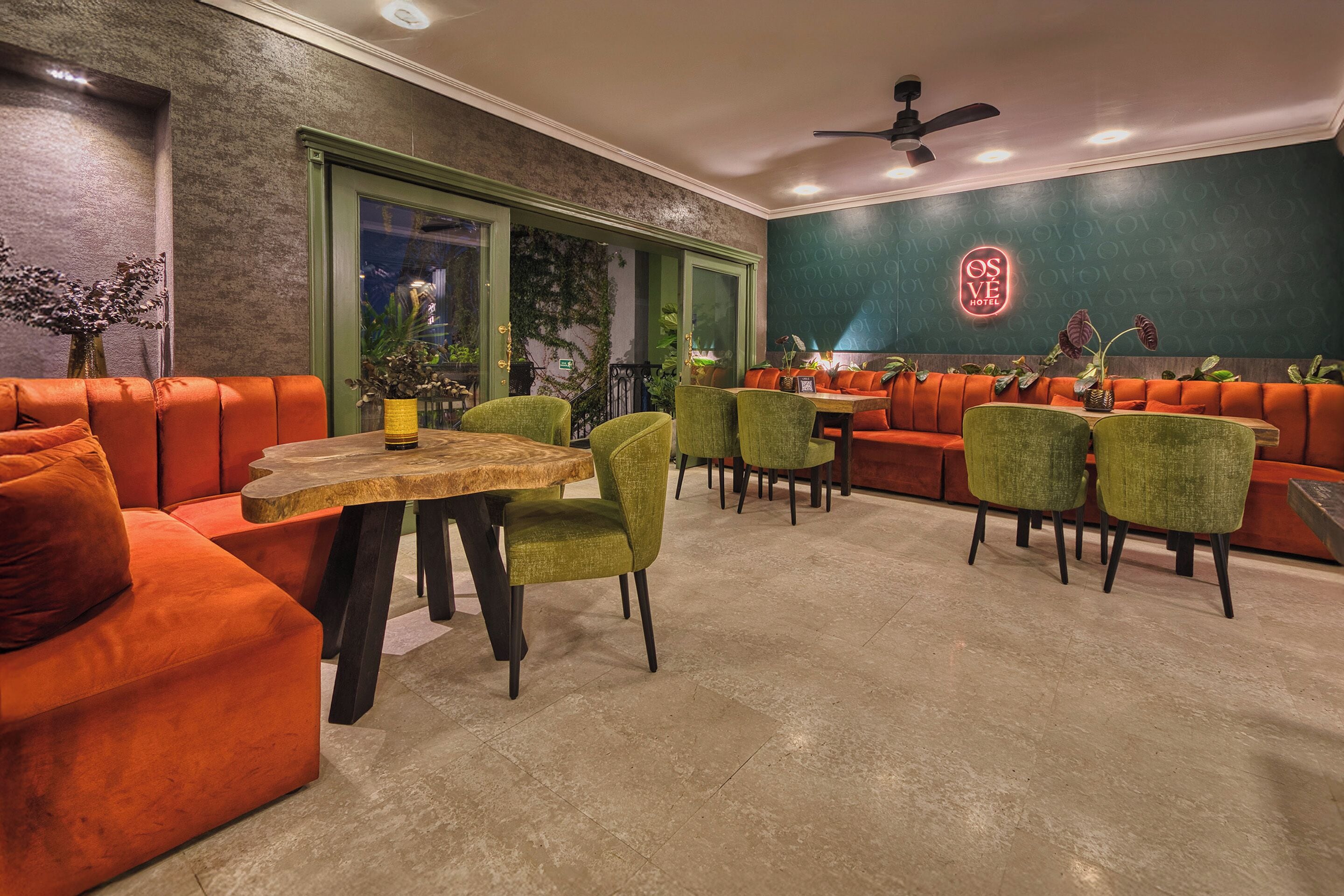 Un espace intérieur accueillant avec des canapés confortables recouverts d’un tissu orange et vert, une table en bois et un panneau lumineux au néon sur le mur.