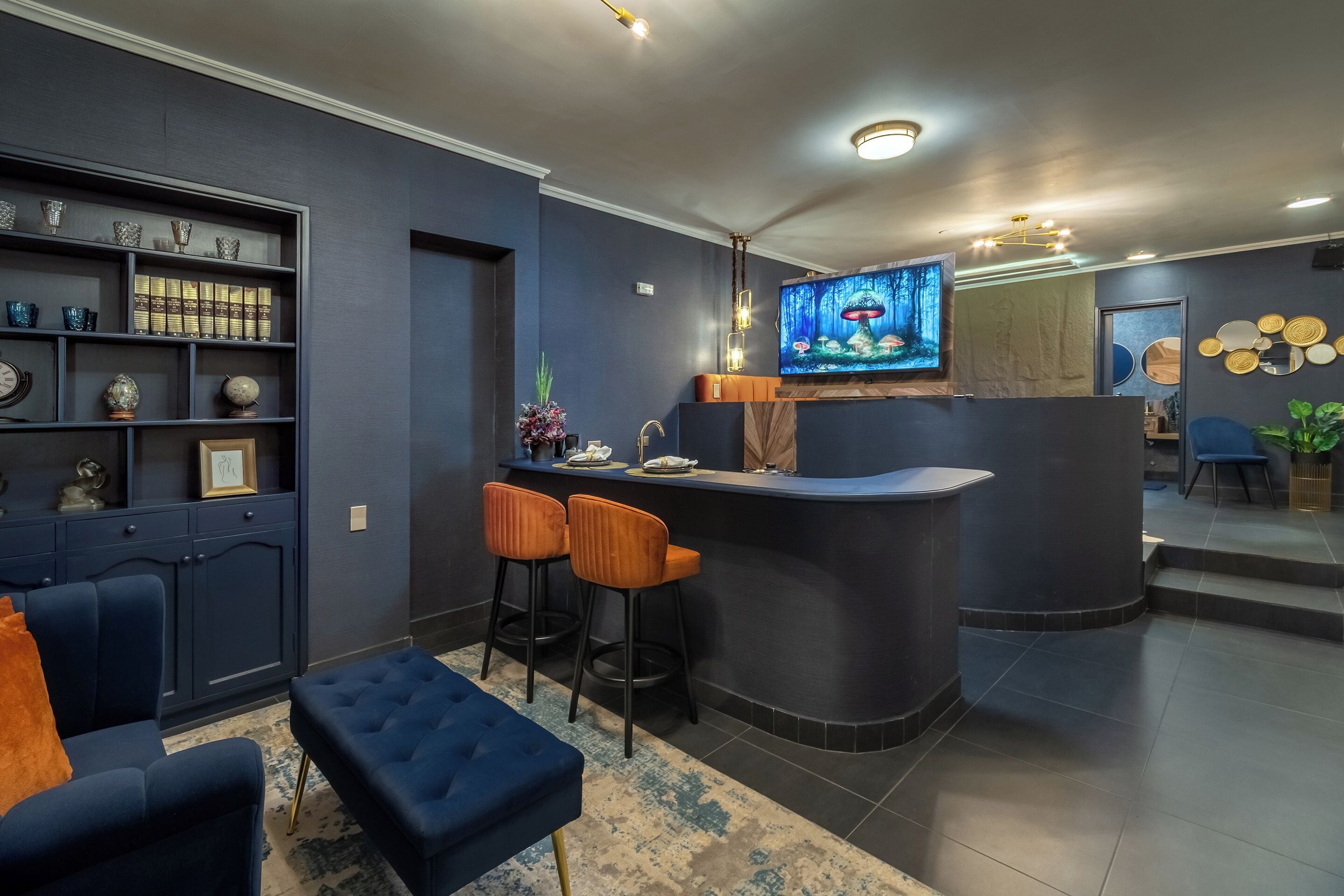 A modern living room with a dark blue sofa, a blue ottoman, and a bar area with two stools.