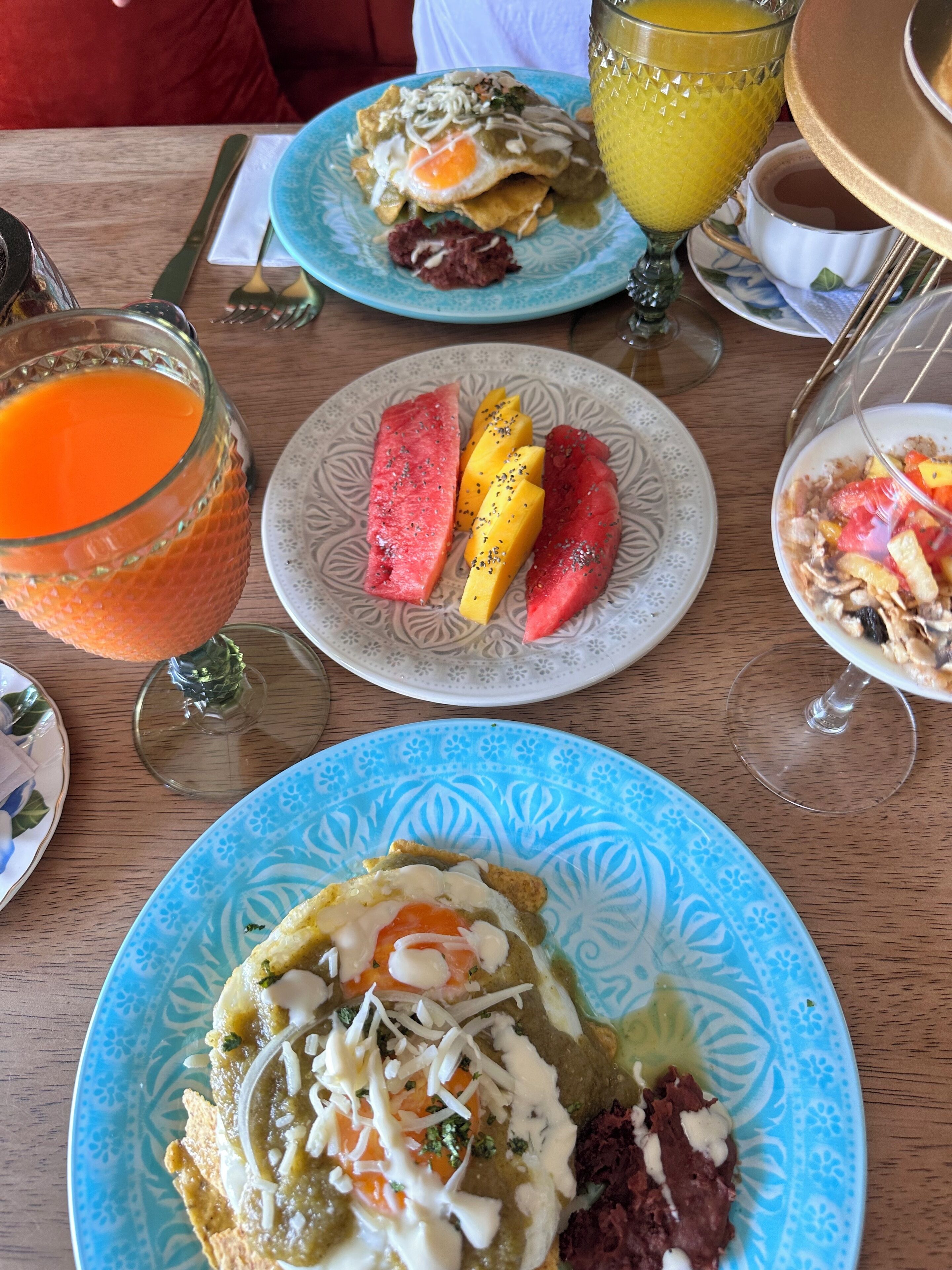 Een tafel met diverse gerechten, waaronder een bord met een gebakken ei, een bord met gesneden fruit, en een glas sinaasappelsap.