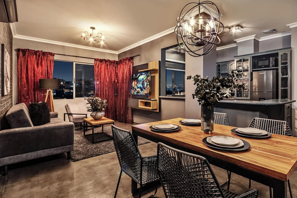 A modern living room with a dining area, a TV, and a kitchen in the background.