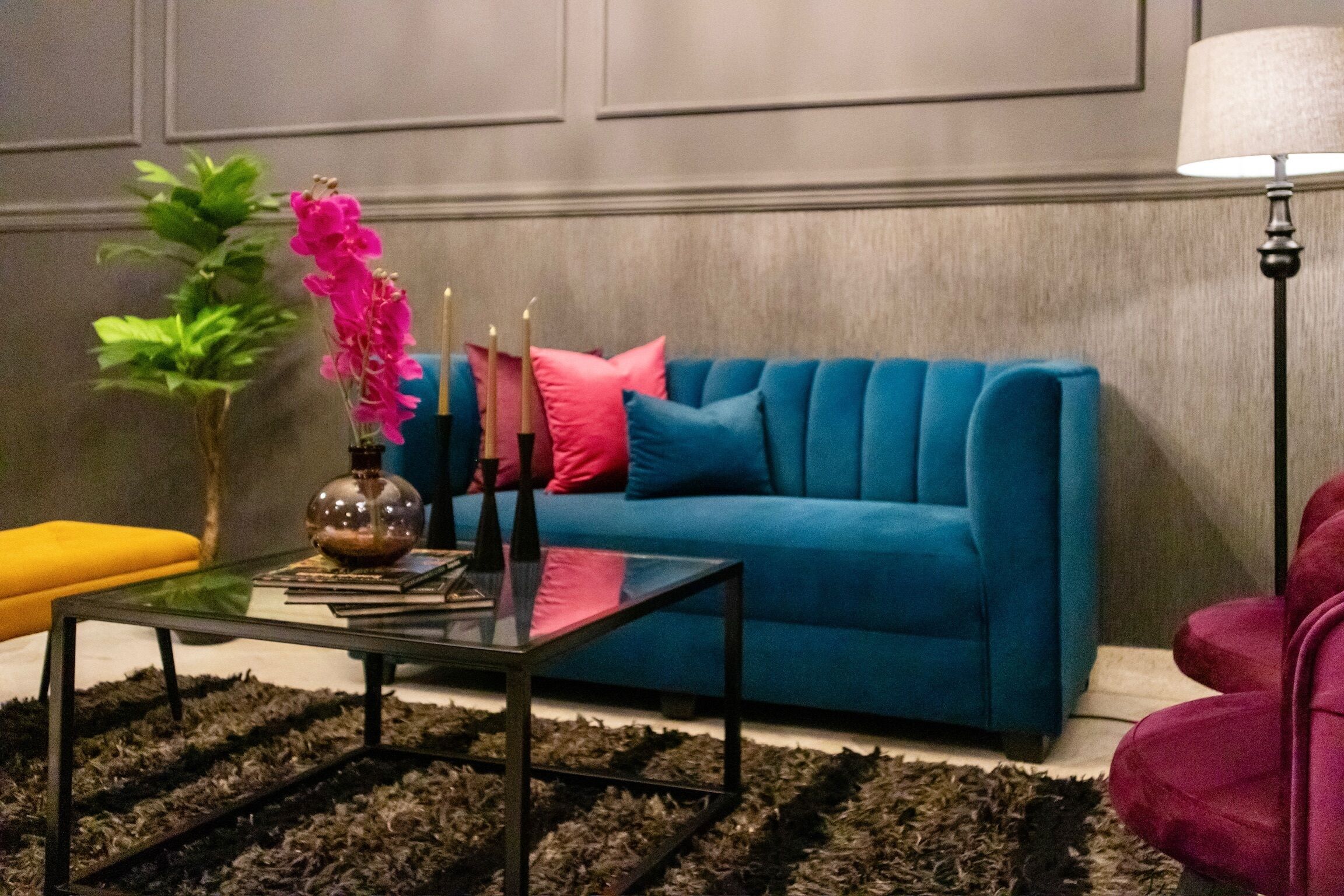 A living room with a blue sofa, a glass coffee table, a plant, and a lamp.