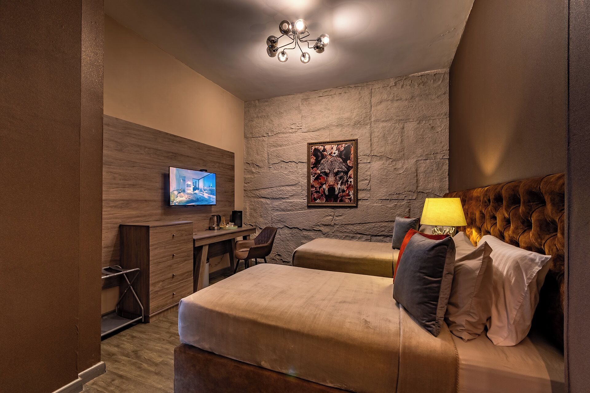 A modern bedroom with a large bed, a desk, a television, and a unique stone wall.