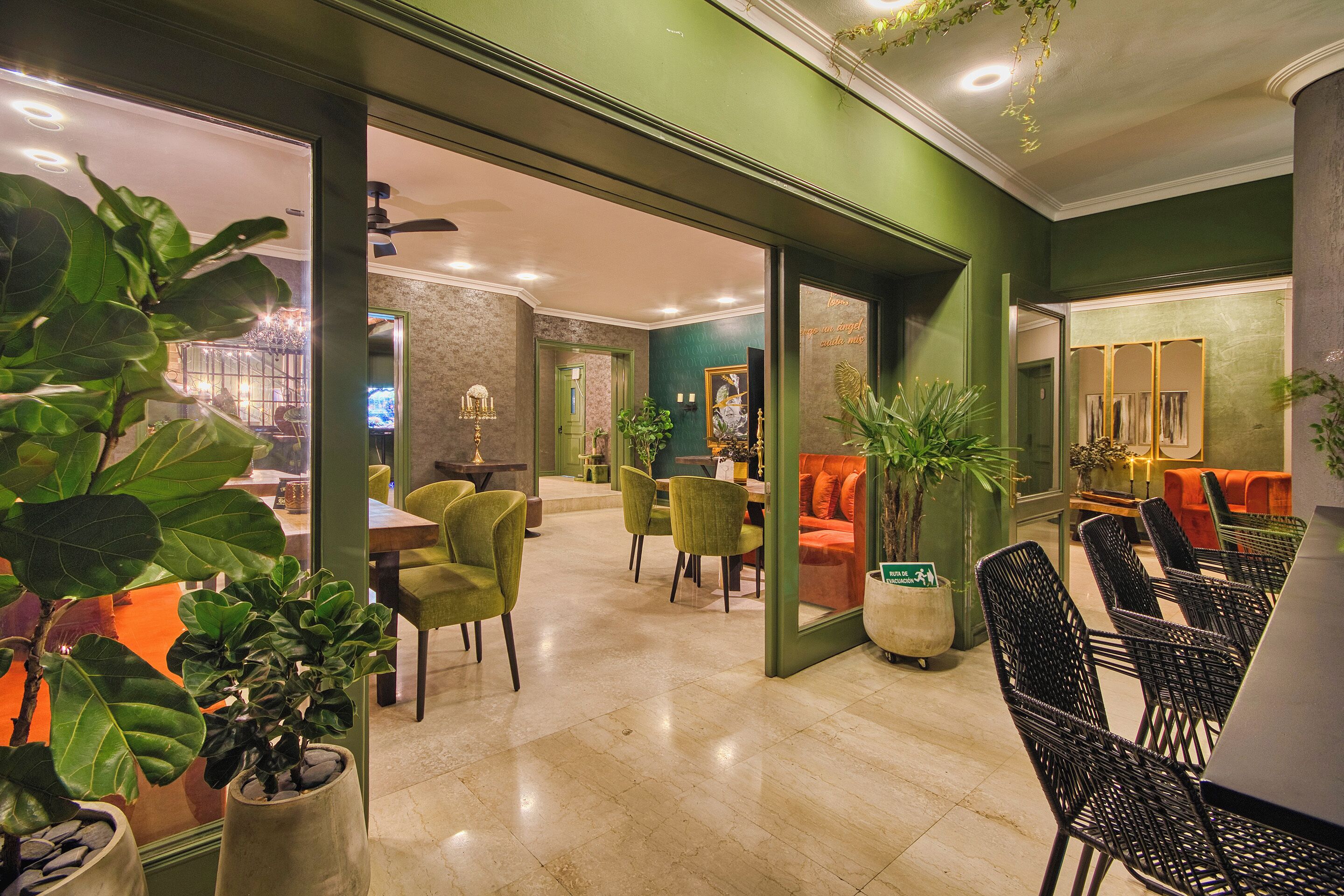A spacious lobby with a green accent wall, a seating area with chairs, a dining table, and potted plants.