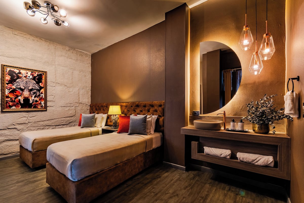 A hotel room with two beds, a large mirror, a vanity with a sink, and a wall-mounted light fixture.