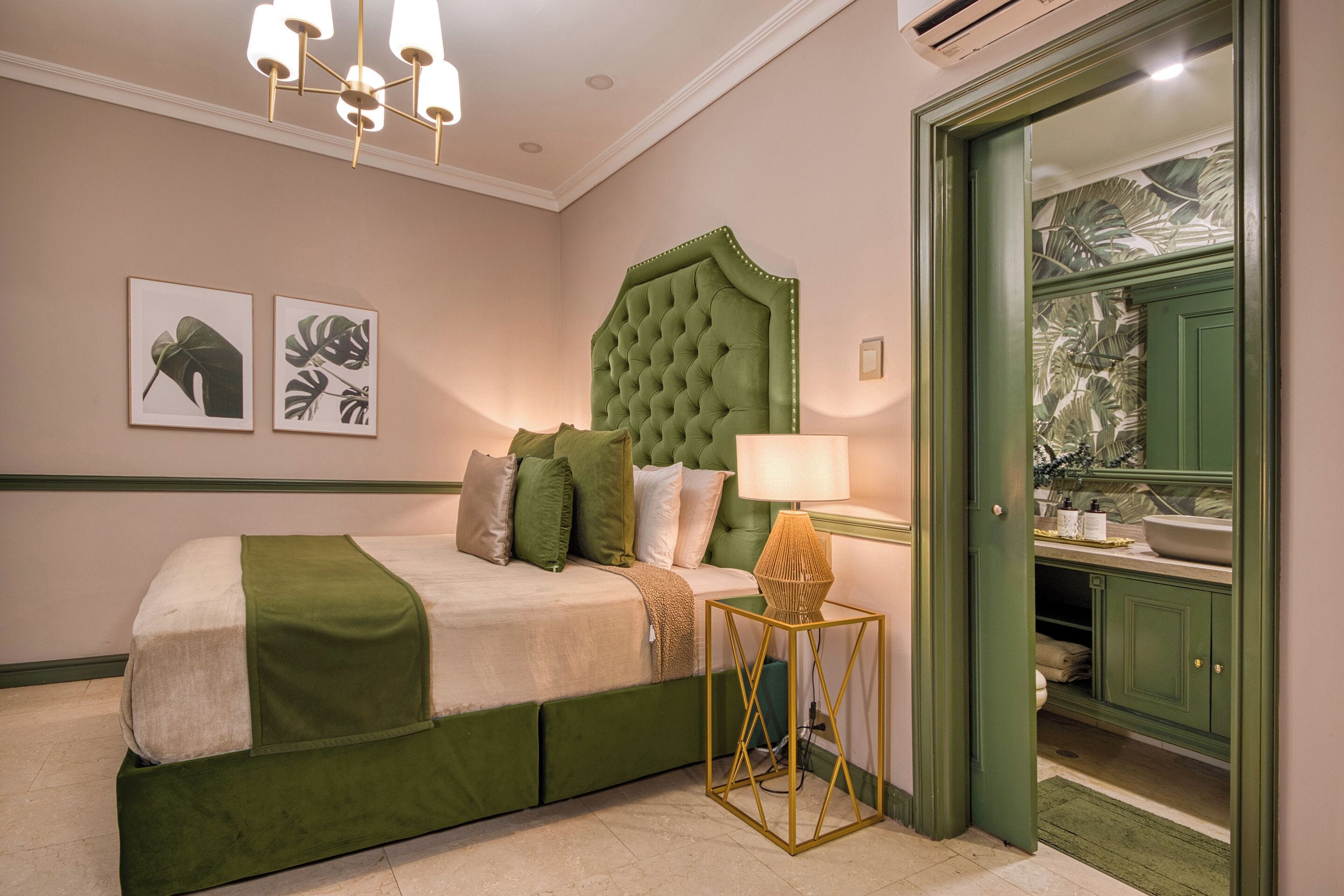A bedroom with a green upholstered bed, a tufted headboard, a bedside table with a lamp, and a green door leading to a bathroom.