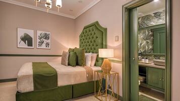 A bedroom with a green upholstered bed, a tufted headboard, a bedside table with a lamp, and a green door leading to a bathroom.