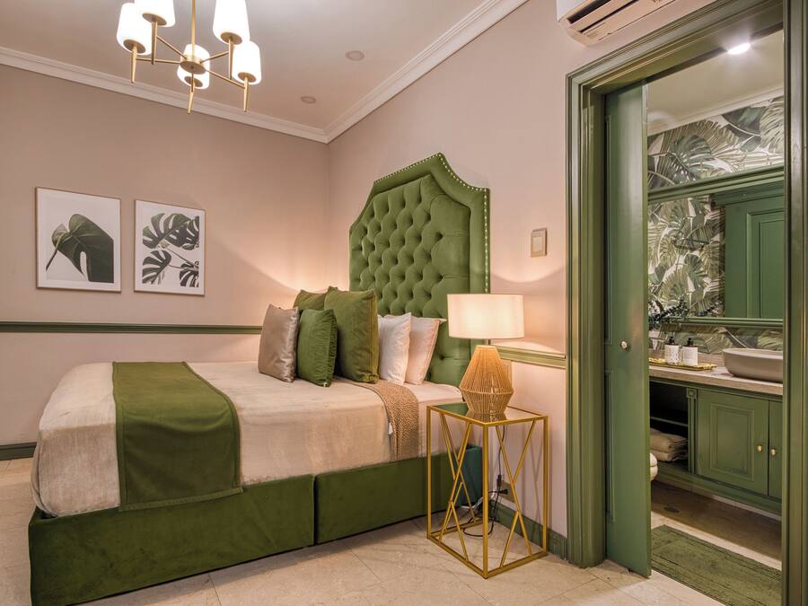 A bedroom with a green upholstered bed, a tufted headboard, a bedside table with a lamp, and a green door leading to a bathroom.