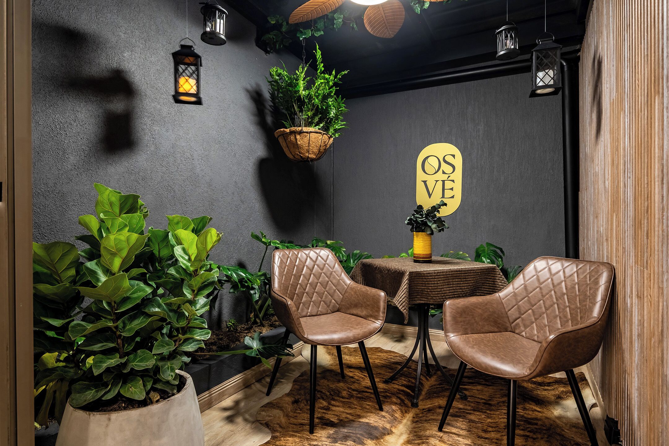 A cozy interior with two leather chairs, a small table, hanging plants, and a wall sign.