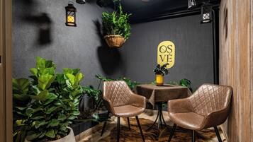 A cozy interior with two leather chairs, a small table, hanging plants, and a wall sign.