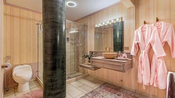 Un baño moderno con ducha de vidrio, tocador con espejo y dos albornoces rosas colgados de ganchos.