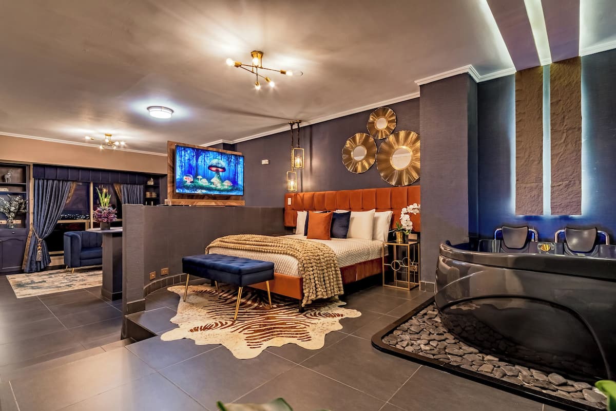 A modern hotel room with a large bed, a seating area, a TV, and a spa tub.