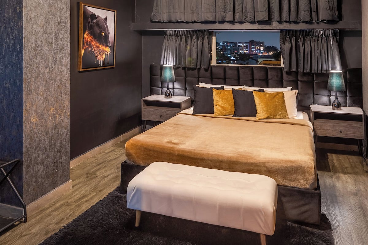 A modern bedroom with a large bed, two bedside tables, a bench, a city view, and a framed picture on the wall.