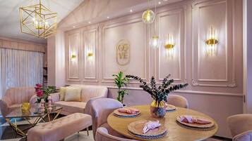 A dining area with a round table, pink upholstered chairs, and a central vase with flowers.