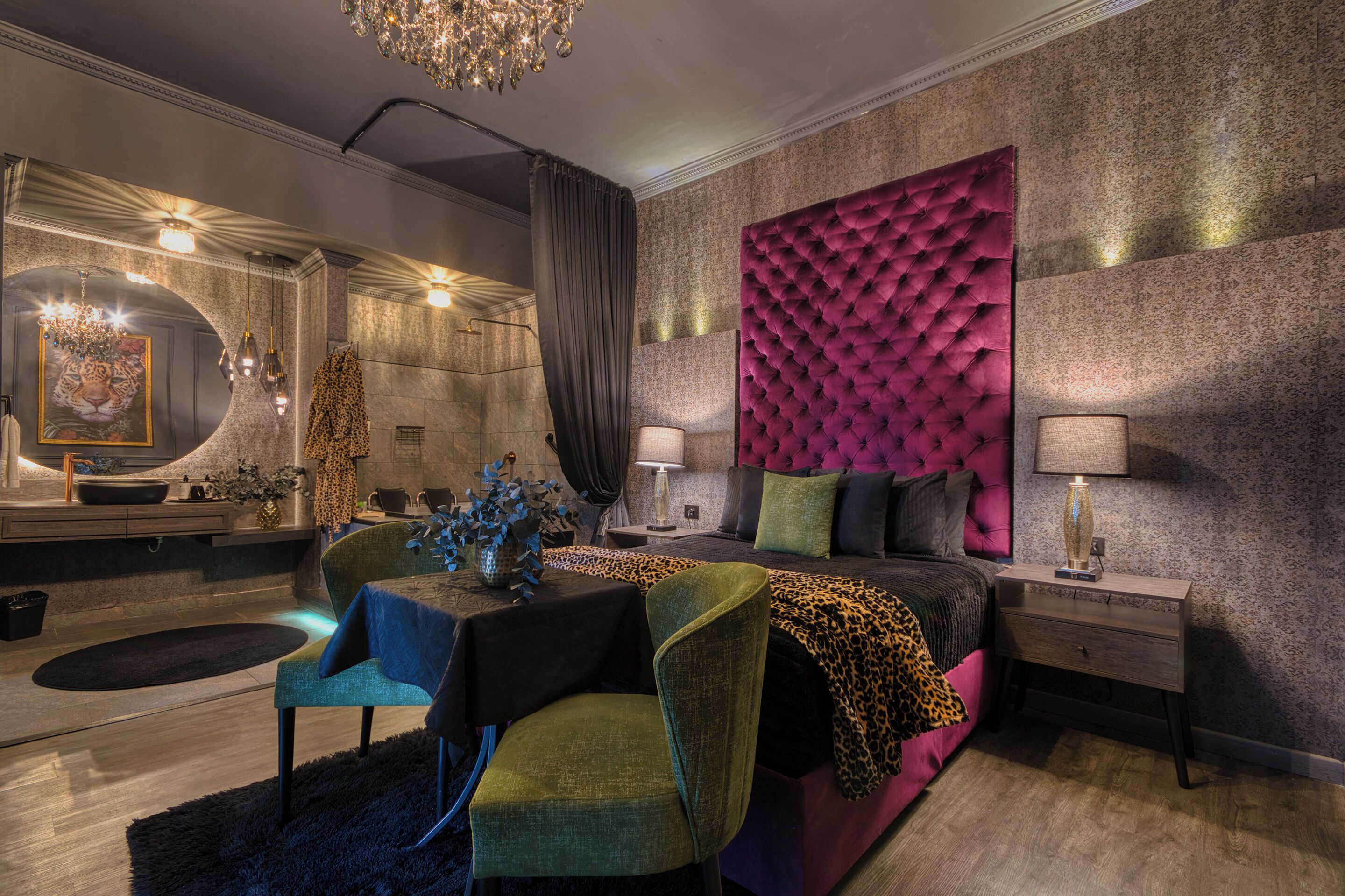 A modern bedroom with a tufted headboard, a round mirror, a chandelier, and a dining area with a table and chairs.