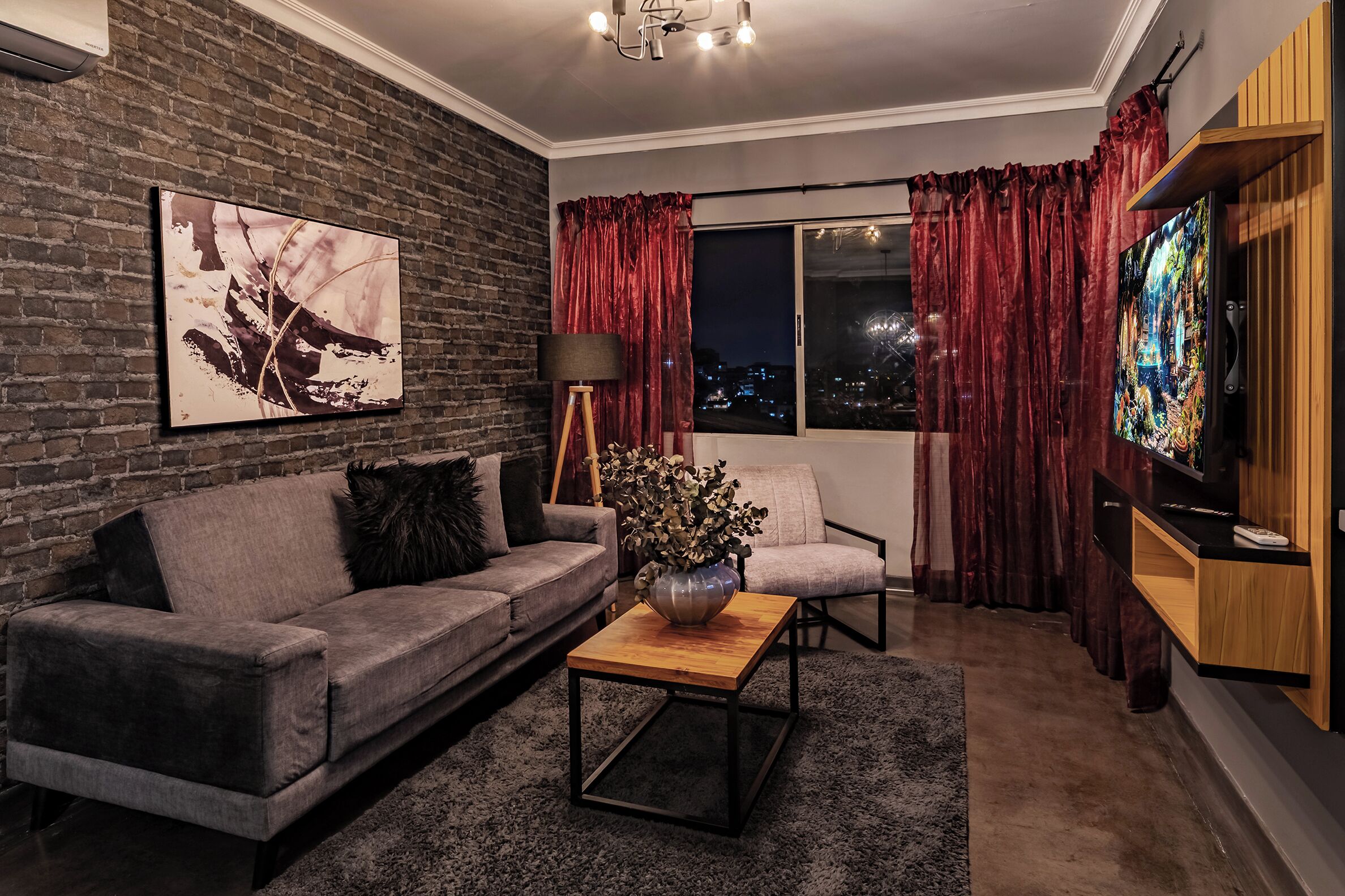 A modern living room with a grey sofa, a coffee table, a floor lamp, and a TV on a wooden stand.