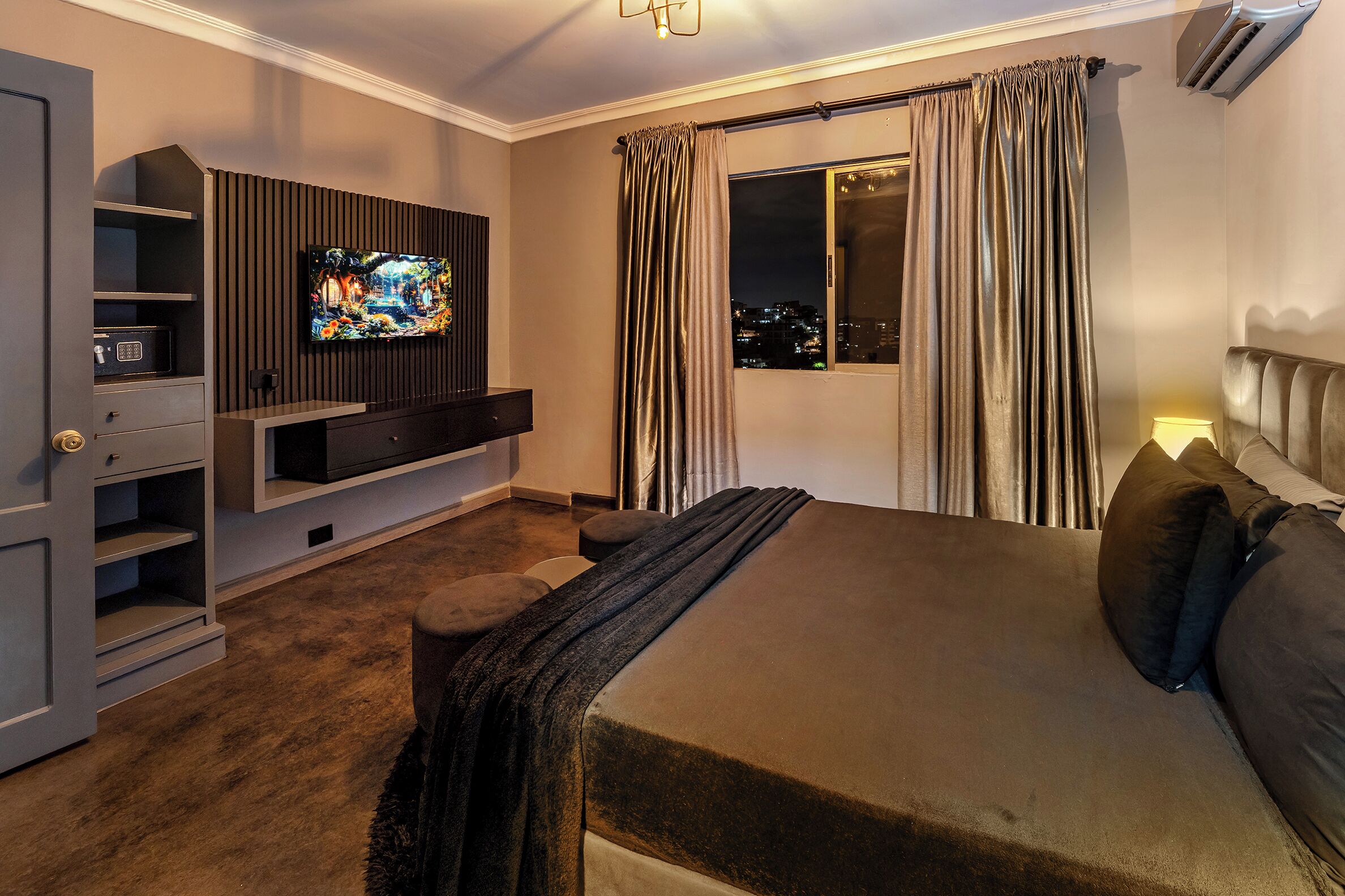 Et moderne hotelværelse med en stor seng, et fladskærms-tv monteret på væggen, et vindue med gardiner og en indbygget tv-reol.