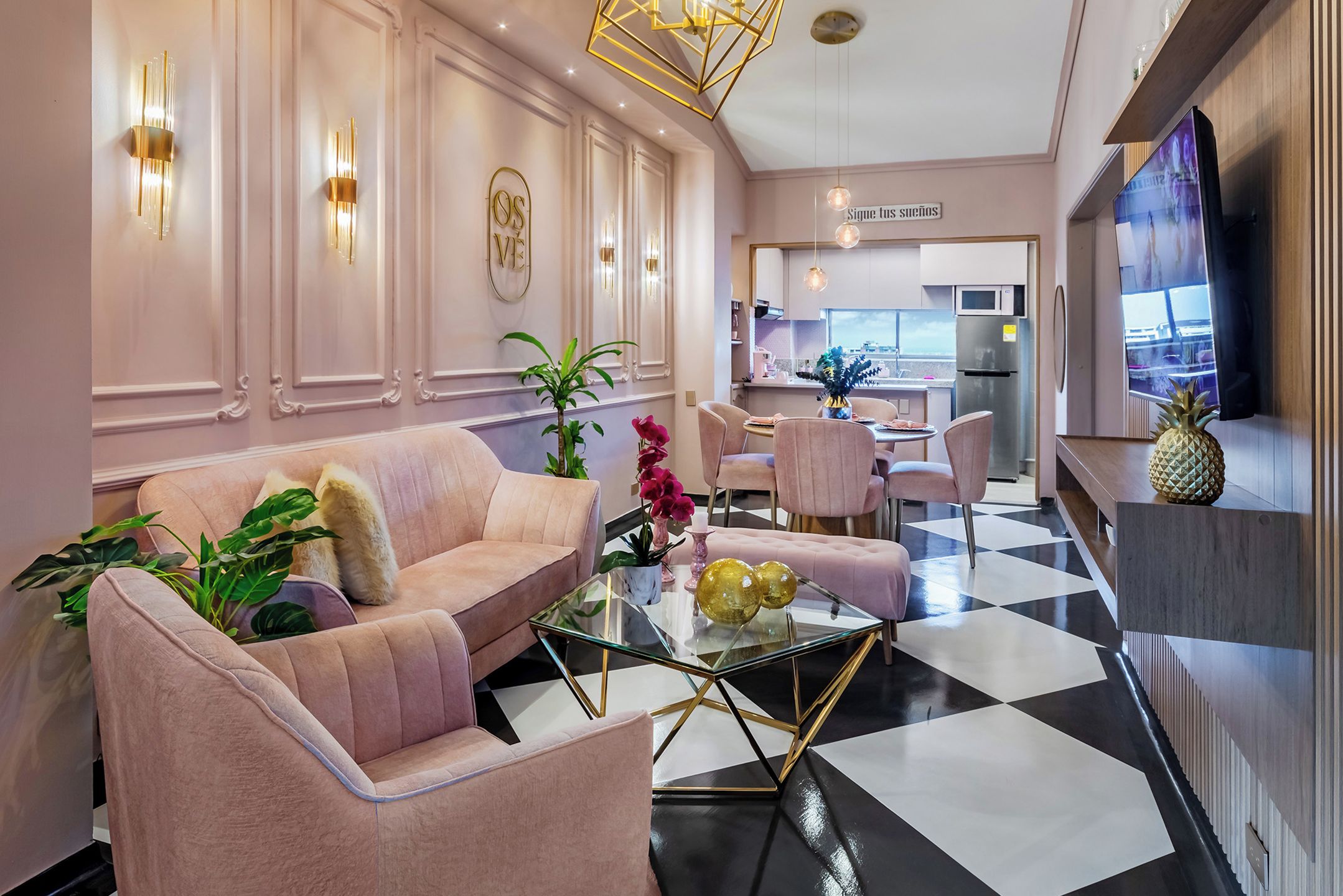 Una sala de estar moderna con una mesa de centro de vidrio, sofás rosados y una cocina al fondo.