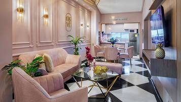 Una sala de estar moderna con una mesa de centro de vidrio, sofás rosados y una cocina al fondo.