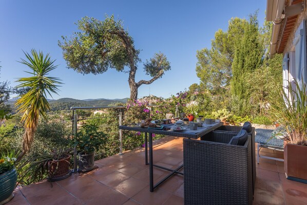 Une terrasse avec une table dressée pour le repas, entourée de plantes en pot et offrant une vue sur la campagne.