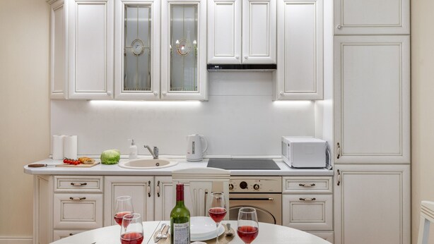 A modern kitchen with white cabinetry, a dining table set with plates, glasses, and a bottle of wine. - Comfortable apartments in Minsk's Mayak (Minsk)