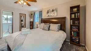 Une chambre avec un grand lit, un ventilateur de plafond, une bibliothèque et une fenêtre avec des rideaux.