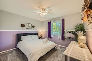 A bedroom with a bed, a ceiling fan, a window with purple curtains, and a nightstand with a lamp. - Pet + Family Friendly | Office | 30 Day | Longmont (Longmont)
