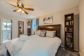 A bedroom with a large bed, a ceiling fan, a bookshelf, and a window with curtains. - Pet + Family Friendly | Office | 30 Day | Longmont (Longmont)