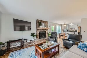 A living room with a fireplace, a flat-screen TV, and a dining area with a kitchen in the background. - Pet + Family Friendly | Office | 30 Day | Longmont (Longmont)