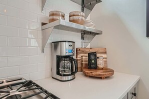A kitchen with a coffee maker, a shelf with bread, and a wooden cutting board.