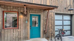 Fachada de madeira com uma porta azul-turquesa, uma bicicleta e uma porta de garagem.