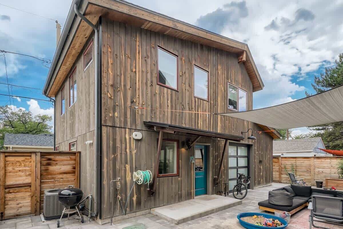 Una casa a due piani in legno con garage, portico coperto e posti a sedere esterni.