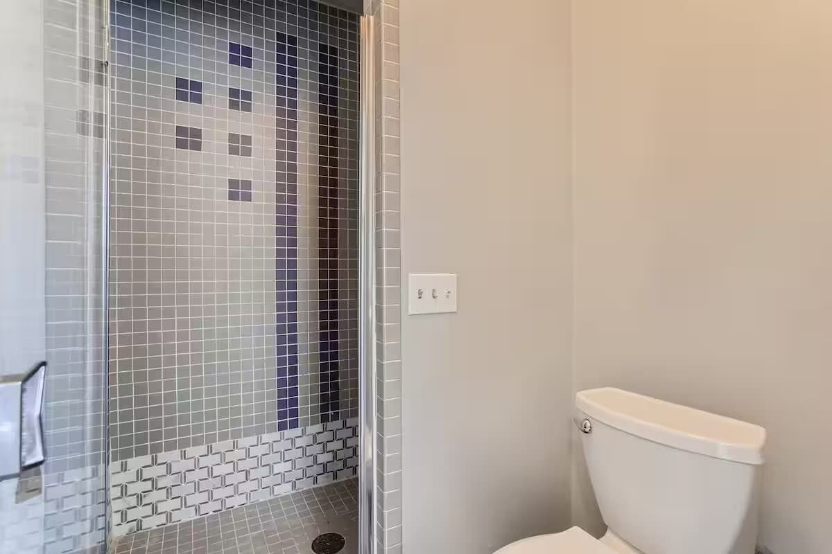 Un baño con cabina de ducha azulejada, un inodoro y un interruptor de luz en la pared.