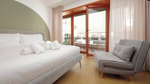 A modern hotel room with a large bed, a grey sofa, and a balcony with a view. - Suites del Gallo (Rome)