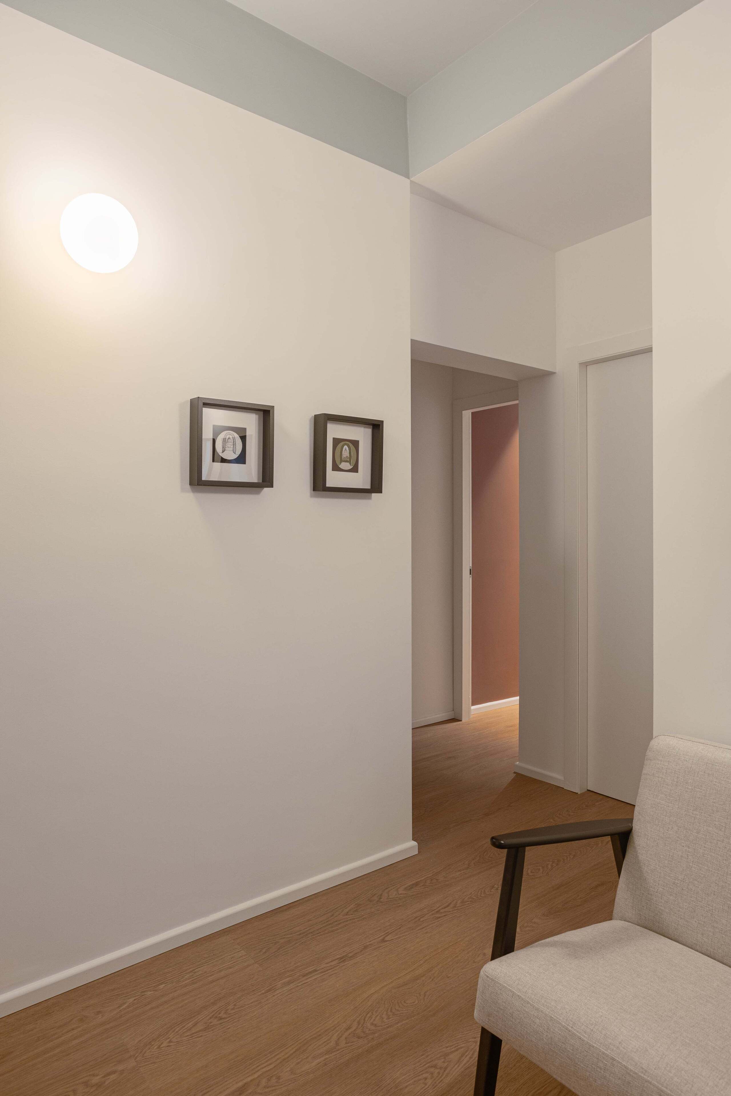 A hallway with two framed pictures on the wall, a chair, and a door leading to another room.