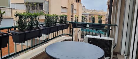 A balcony with a table and potted plants, overlooking a residential area with buildings and a pool.