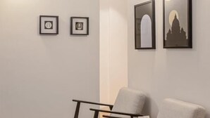 A modern waiting area with two grey chairs, a wooden floor, and framed artwork on the wall. - Suites del Gallo (Rome)