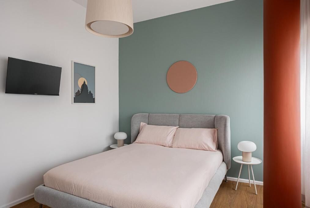 Une chambre à coucher comprenant un lit, un téléviseur, un tableau accroché au mur, un miroir rond et une table de chevet.