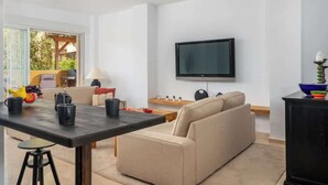 Ein modernes Wohnzimmer mit einer Couch, einem Couchtisch, einem an der Wand montierten Fernseher und einem Essbereich mit Tisch und Stühlen.