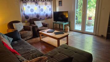 Een woonkamer met een bank, fauteuils, een salontafel, een televisie en een glazen schuifdeur die uitkomt op een buitenruimte.