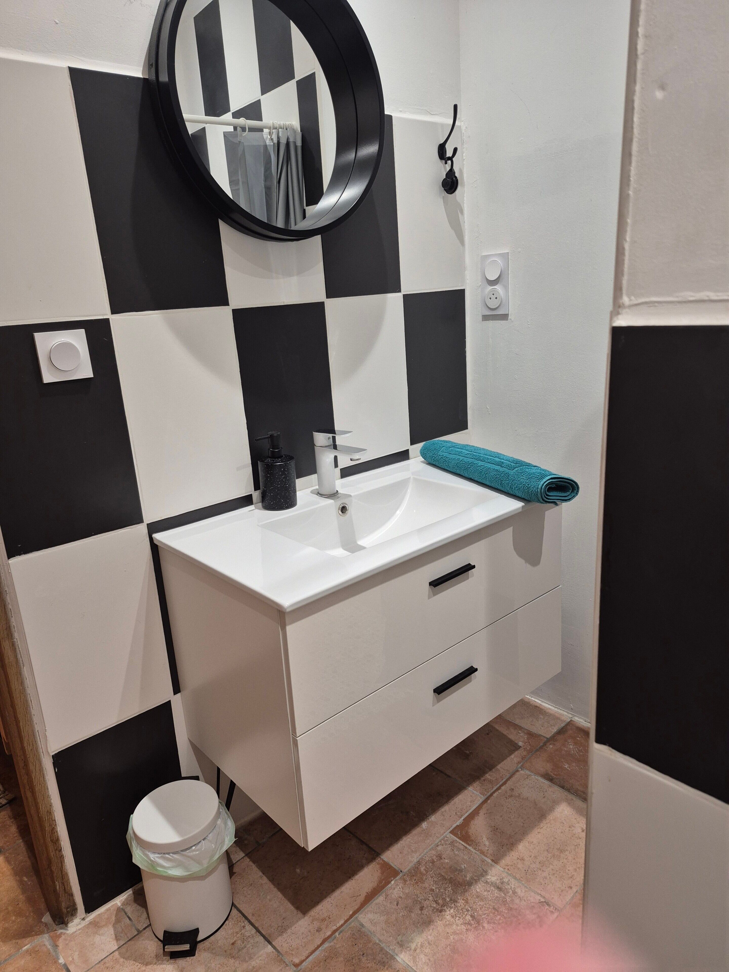 A bathroom with a white sink, black and white checkered tiles, a round mirror, and a towel on the counter.