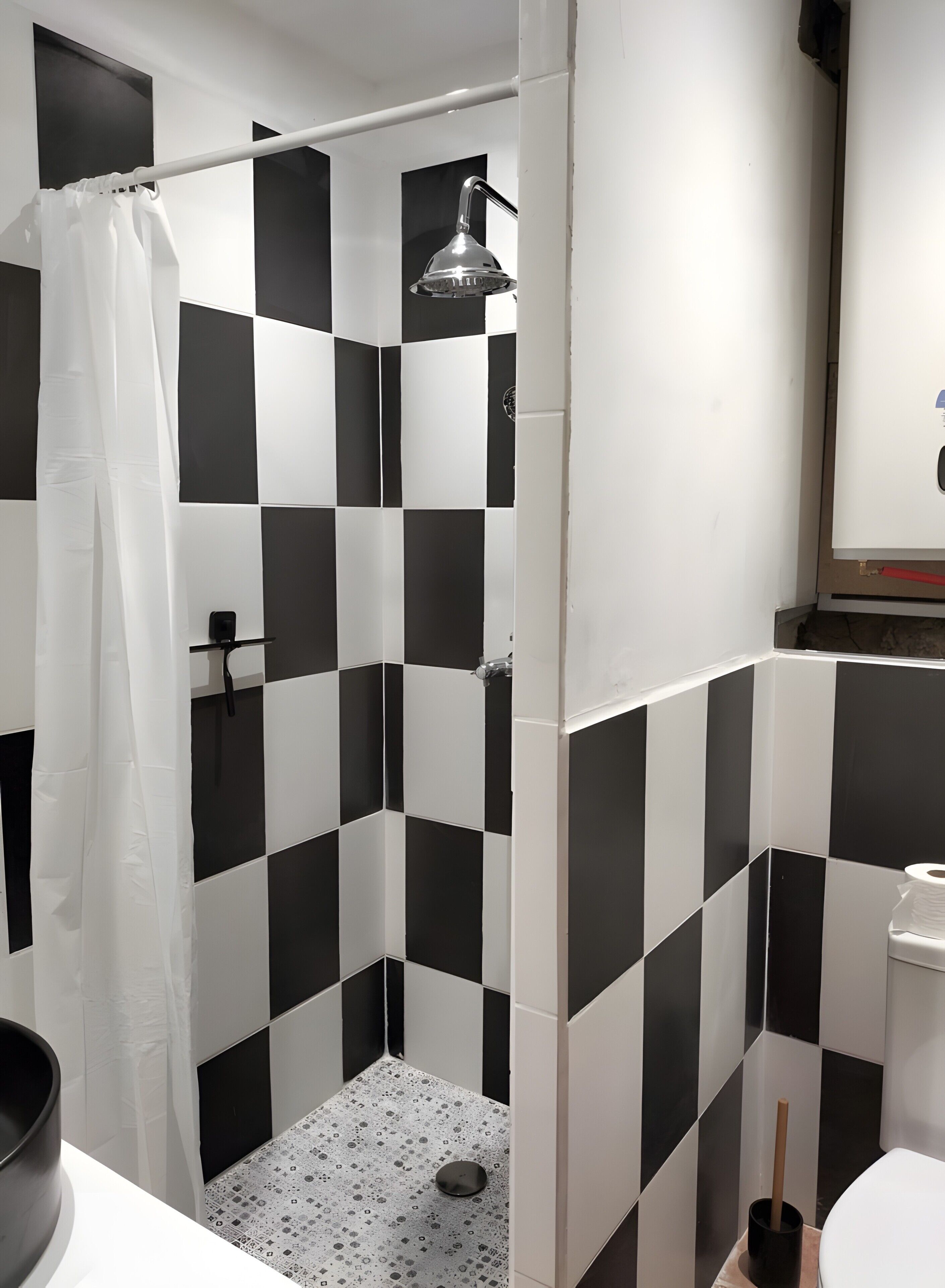 Um banheiro com ladrilhos quadriculados em preto e branco, um chuveiro com porta de vidro, vaso sanitário e pia.