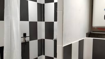 Um banheiro com ladrilhos quadriculados em preto e branco, um chuveiro com porta de vidro, vaso sanitário e pia.