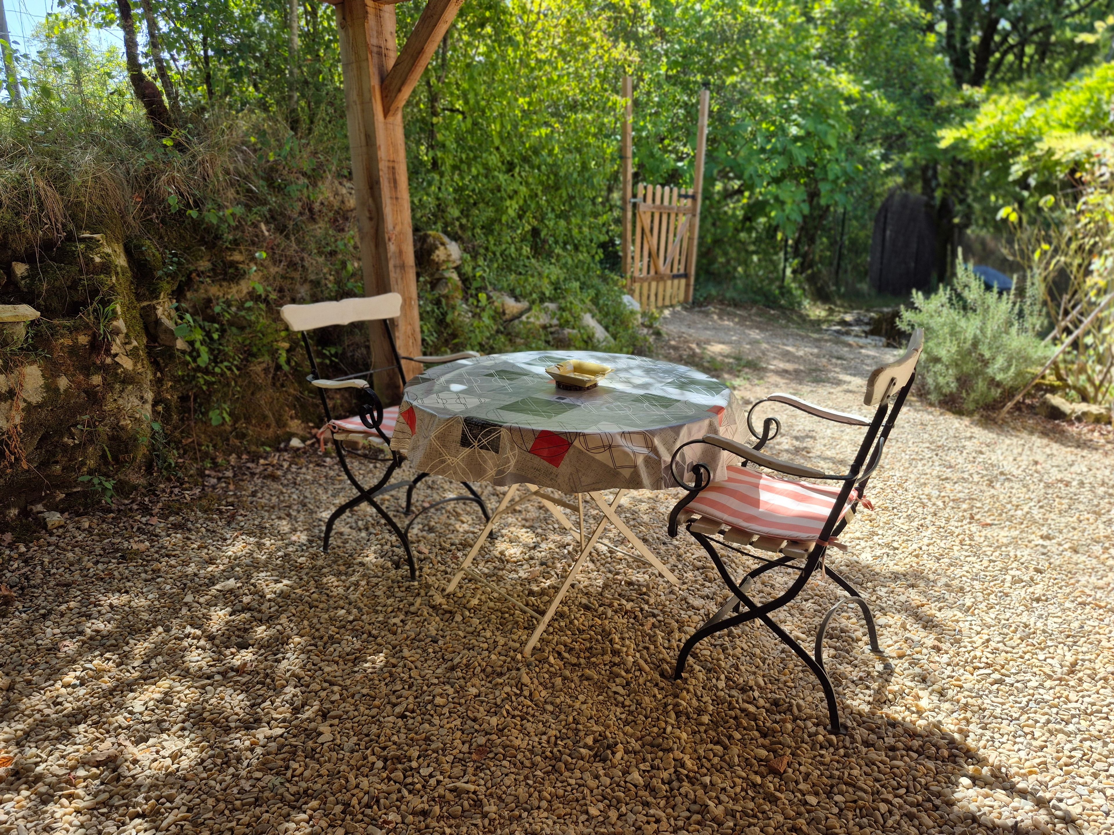 An outdoor seating area with a round table and two chairs, surrounded by gravel and greenery.