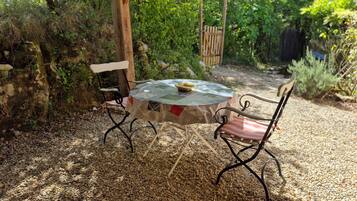 An outdoor seating area with a round table and two chairs, surrounded by gravel and greenery.