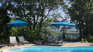 Una piscina con lettini e ombrelloni, circondata da alberi e con vista sulla campagna.